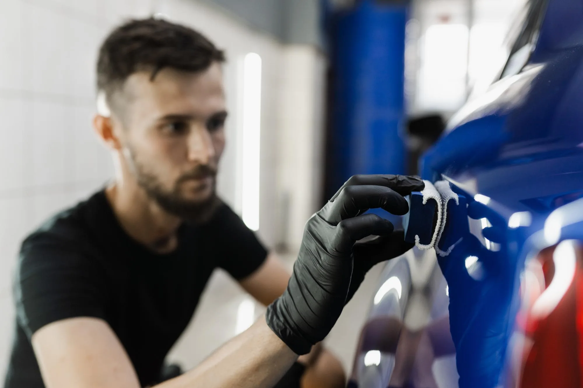 A technician from A1 Mobile Detailing & Ceramic, wearing a black glove, applies a premium nano ceramic coating to the glossy blue exterior of a luxury vehicle.