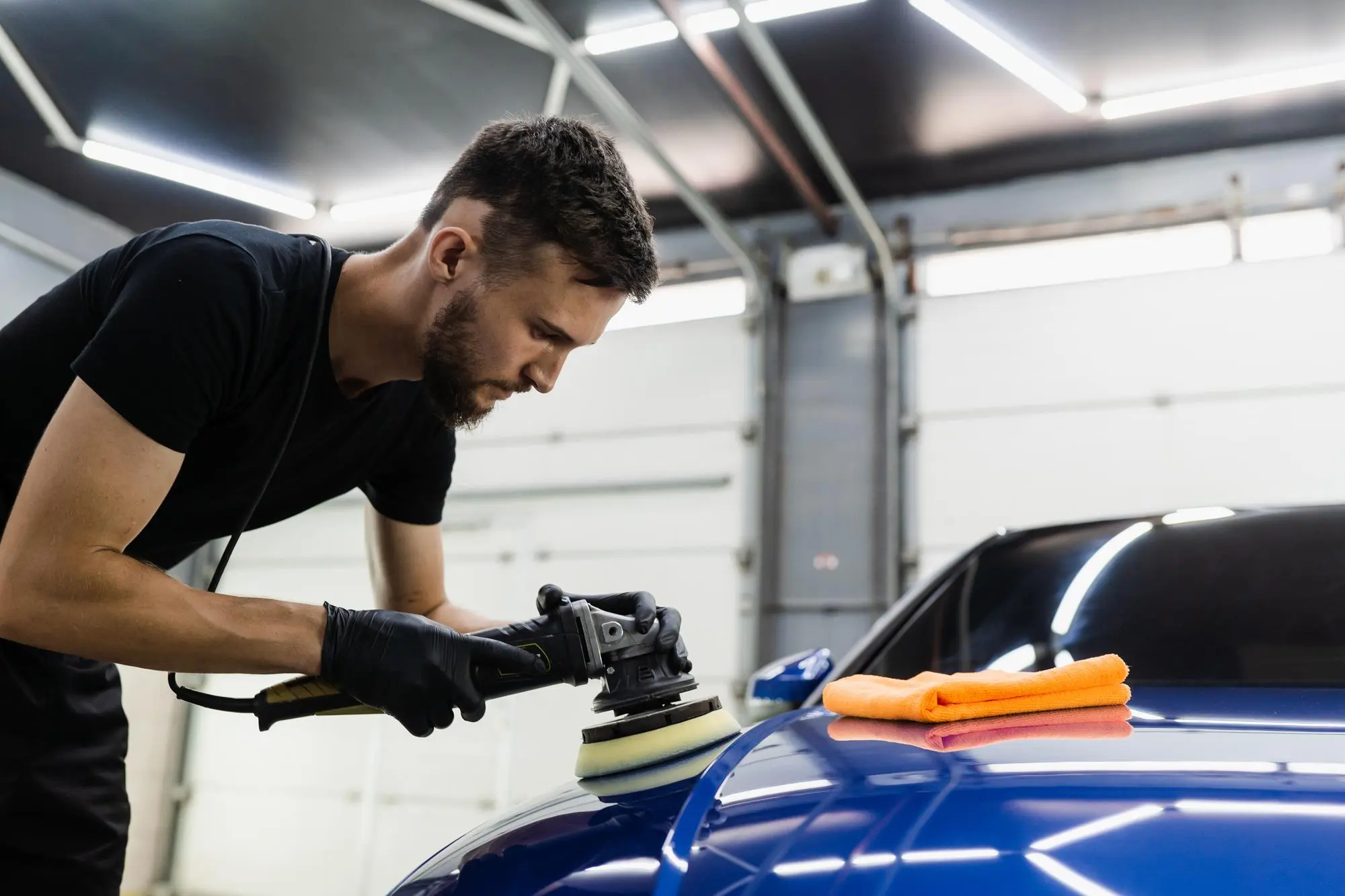 A professional at A1 Mobile Detailing & Ceramic using an orbital polisher to apply a high-gloss Ceramic Wax coating to the hood of a blue luxury car.