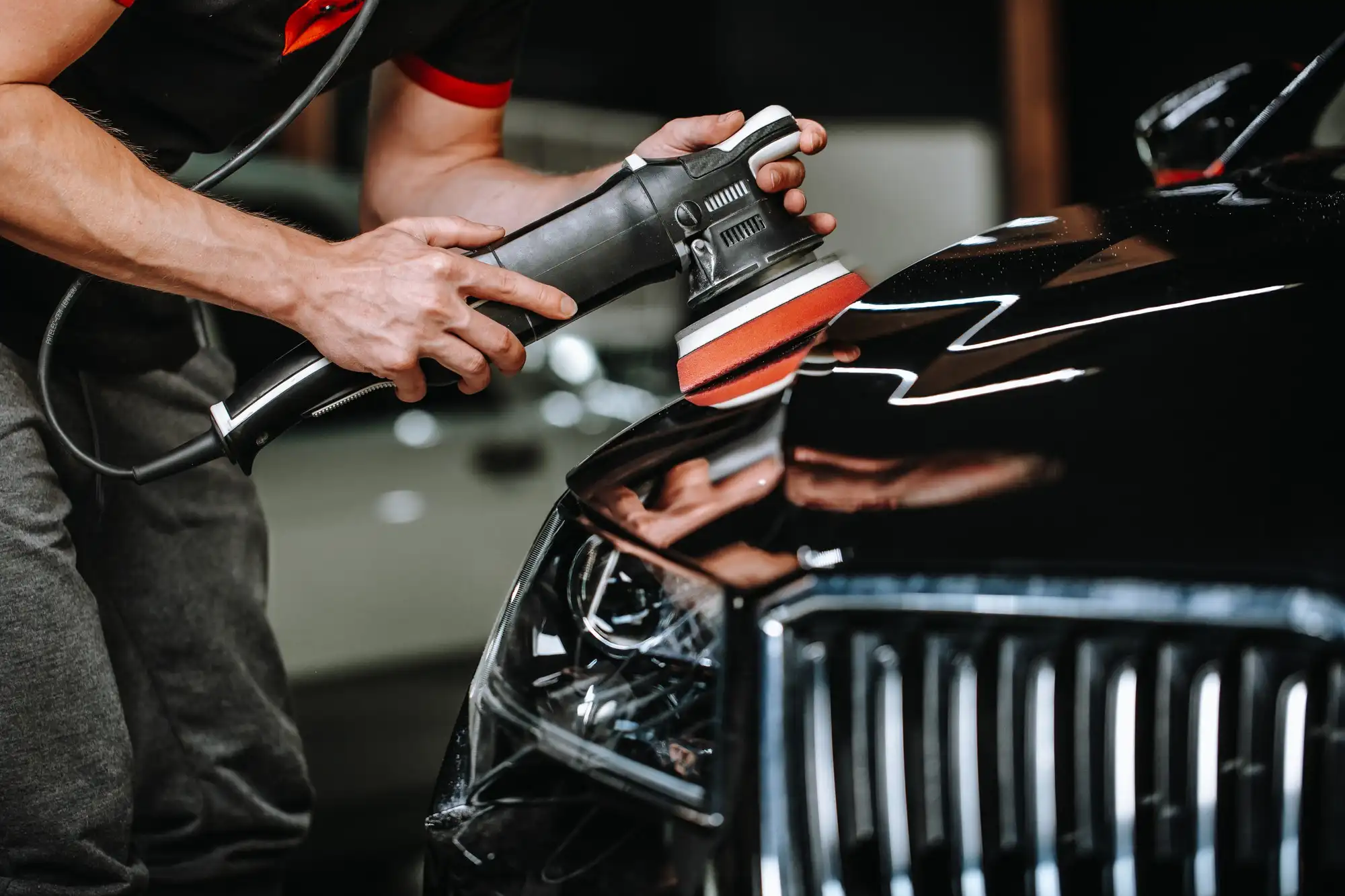 Professional car detailing technician at A1 Mobile Detailing & Ceramic using a dual-action polisher to buff and shine the hood of a black luxury car.