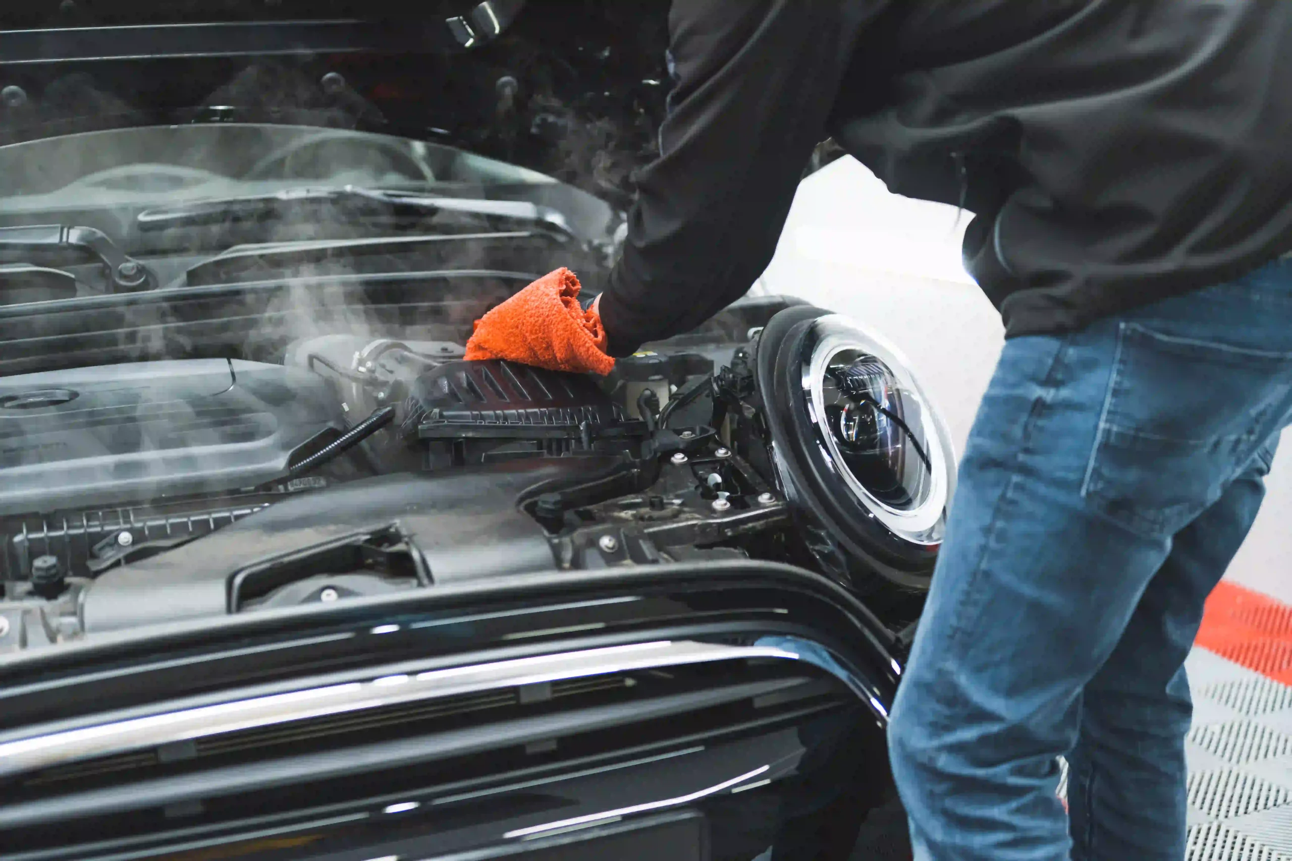 Professional Engine Detailing by A1 Mobile Detailing & Ceramic showing a technician using steam cleaning technology and a microfiber cloth to remove grease and grime from a car engine bay.
