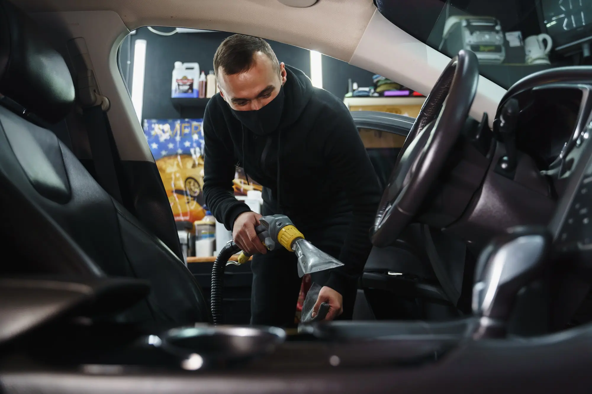 A technician from A1 Mobile Detailing & Ceramic performing deep Interior Car Detailing by using a professional steam extractor on the black leather seats of a vehicle.