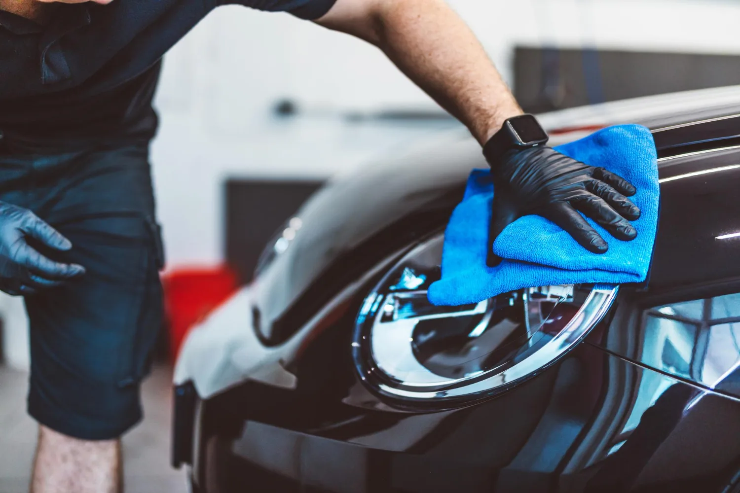 Trust Our Lead Detailer with Your Car as he meticulously wipes down the headlight and hood of a black vehicle using a premium microfiber towel at A1 Mobile Detailing & Ceramic.