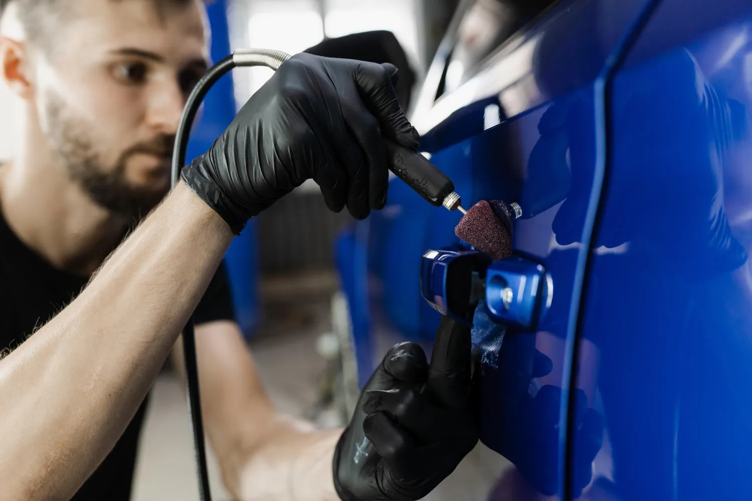 A skilled technician from A1 Mobile Detailing & Ceramic uses a specialized nano-polishing tool to detail the tight areas around a blue car's door handle. Trust A1 Mobile Detailing & Ceramic for high-precision automotive care.