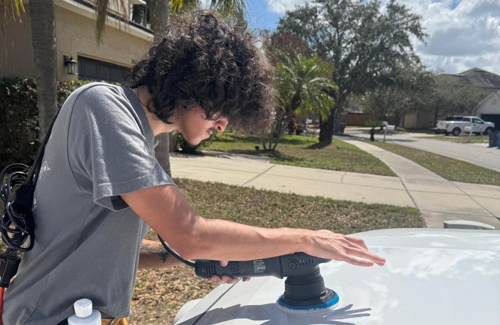 A professional detailer with a power buffer polishing a white car's hood, showcasing precision techniques at a Premium Car Detailing Center in Florida.